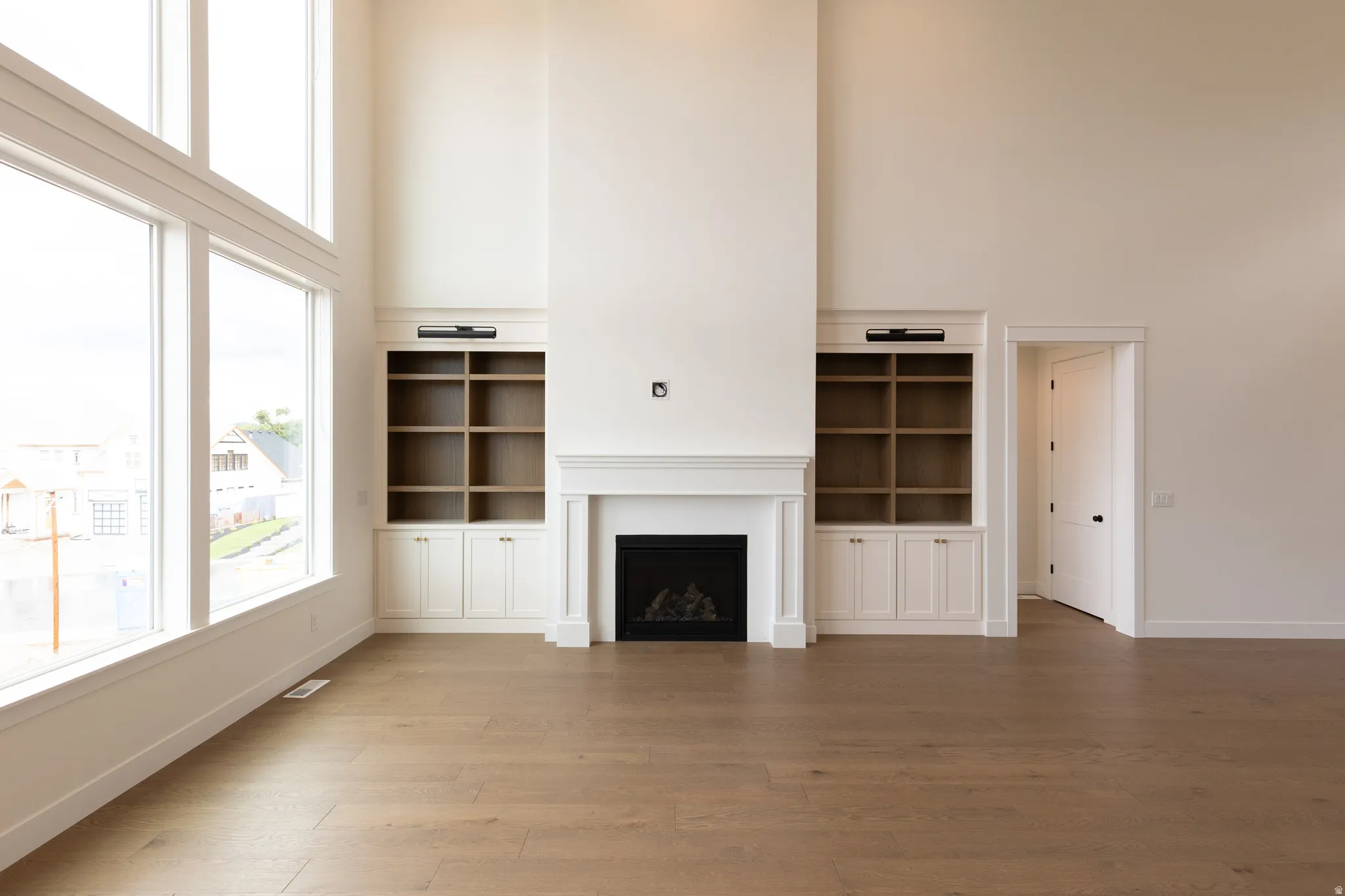 High ceilings with extensive window fenestration, wood-finish flooring, a fireplace with a white mantel, and built-in cabinetry