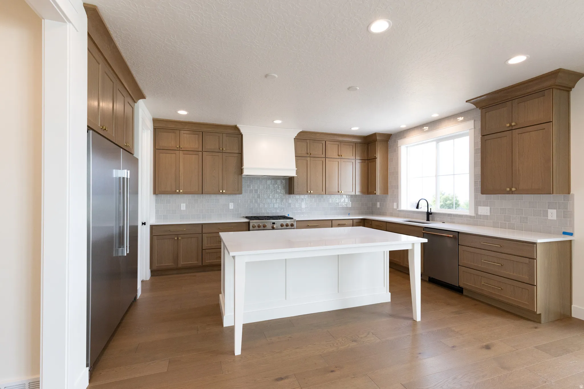 Spacious kitchen featuring light wood-finish cabinetry, a white island, stainless steel appliances, a tile backsplash, and recessed lighting