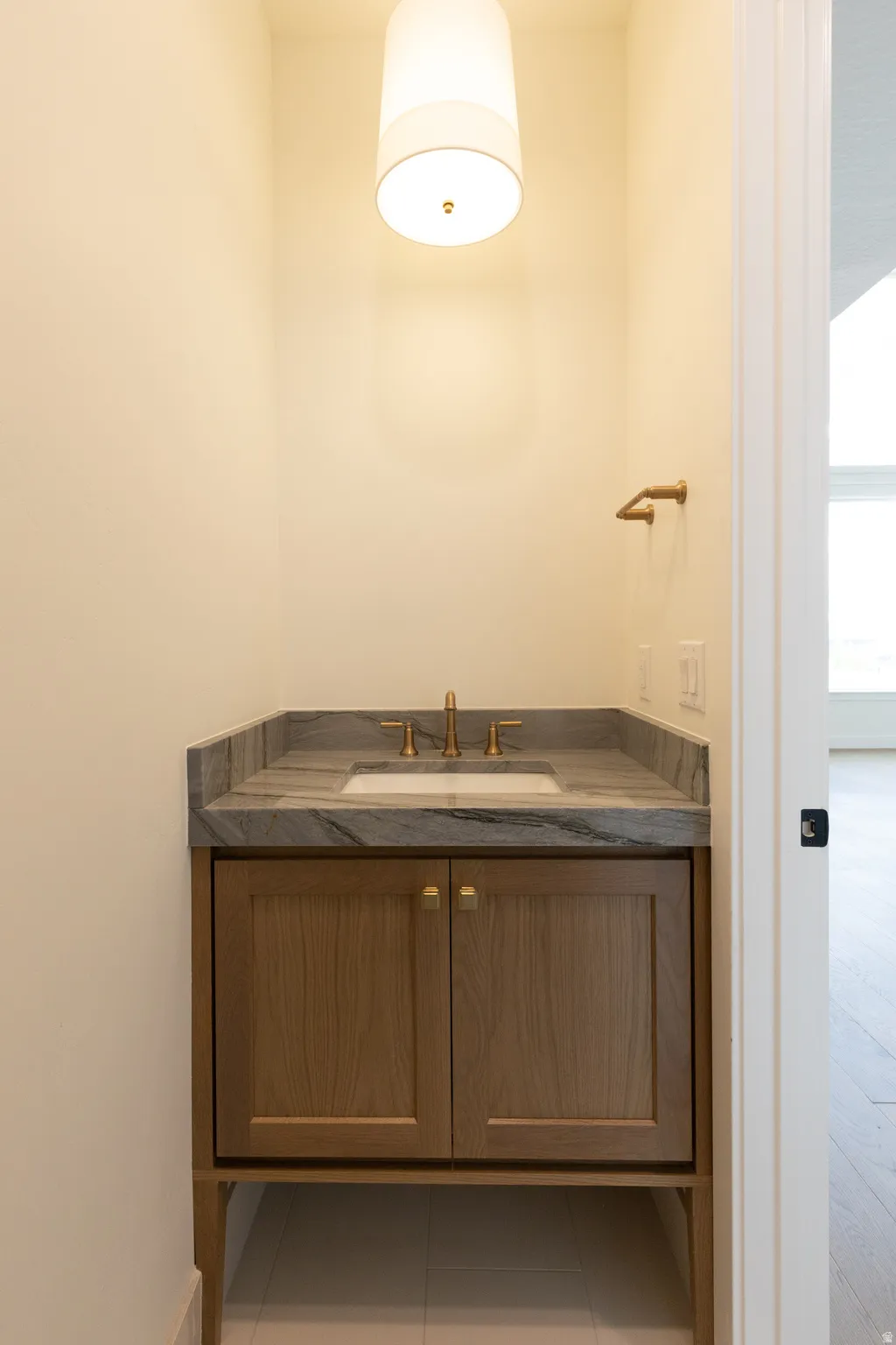Contemporary vanity with a rectangular sink, stone countertop, brass-finish faucet, and wood-finish cabinetry