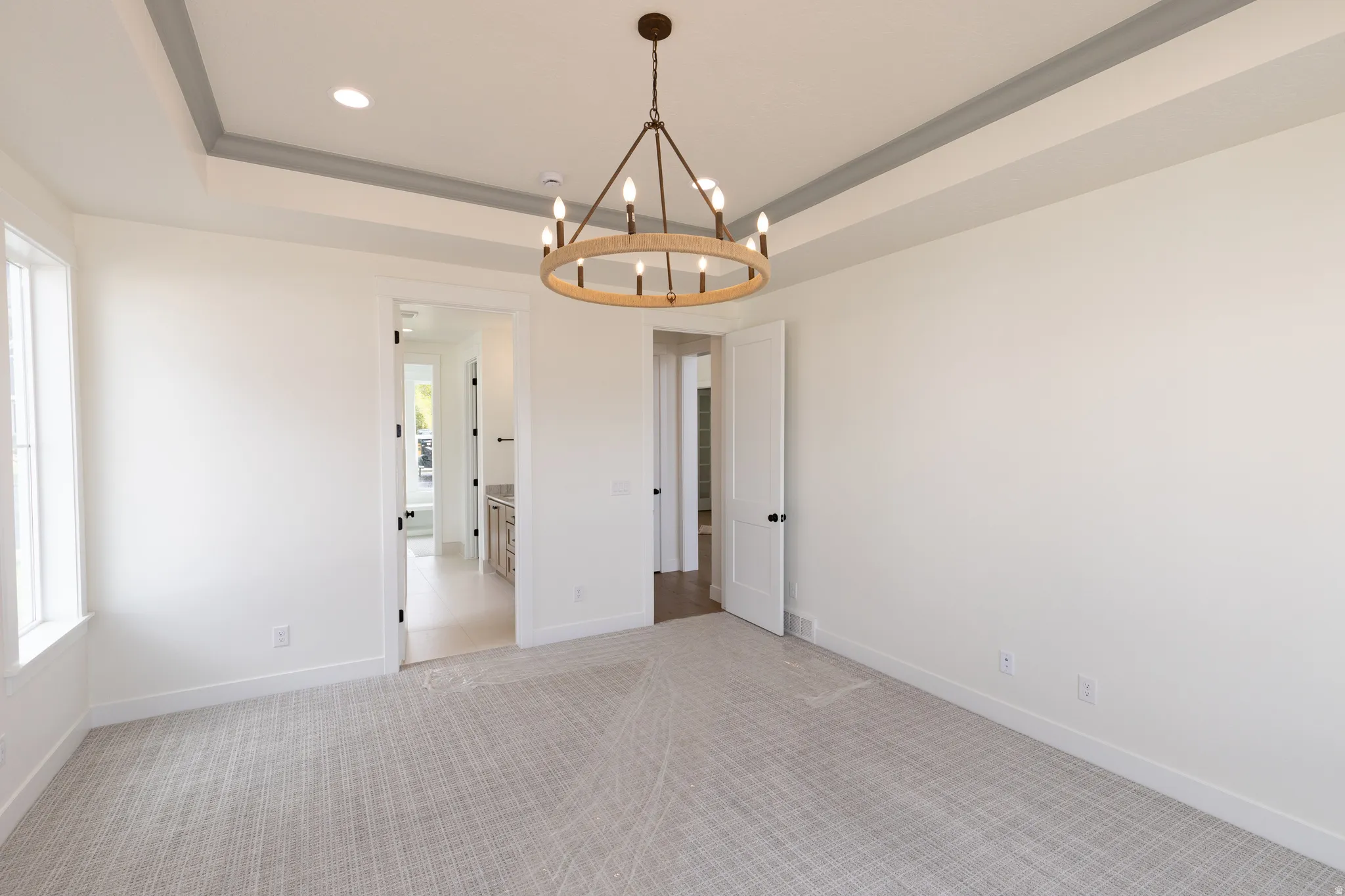 Tray ceiling with recessed lighting, central chandelier, light gray carpeting, and white trim