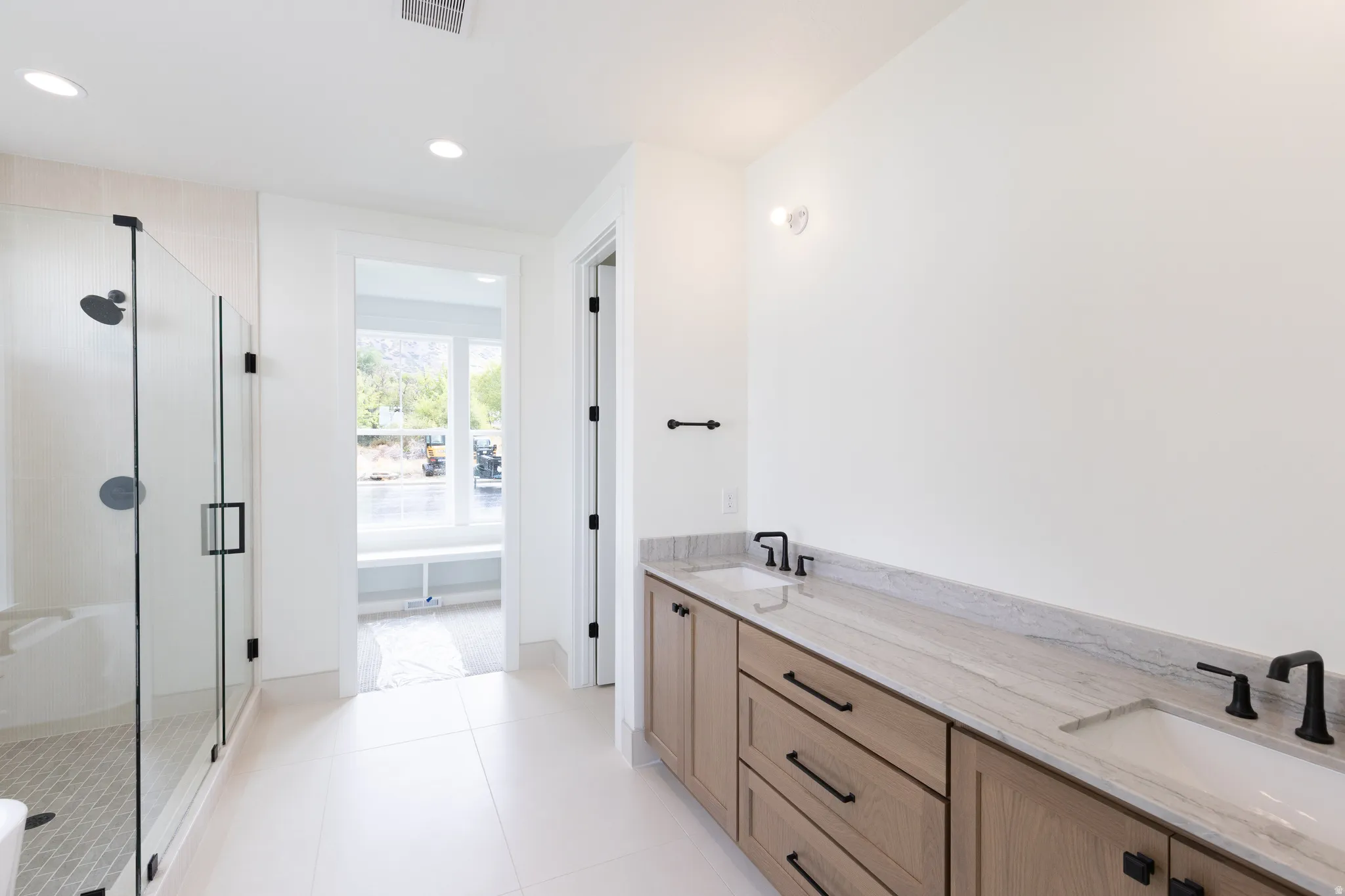Dual vanity with matte black fixtures, light wood-finish cabinetry, and a stone countertop