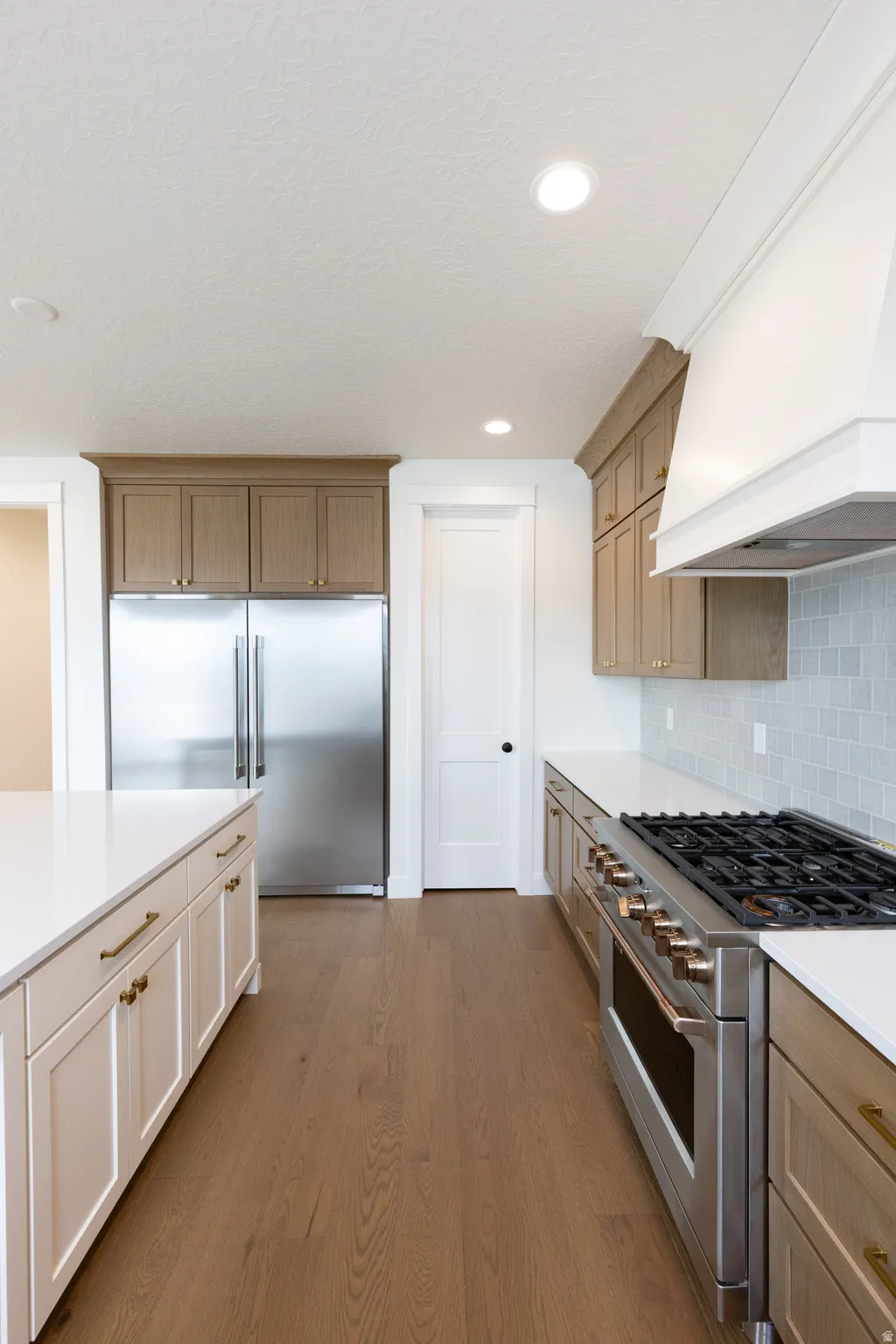 Sleek stainless steel refrigerator, professional-grade range, light wood-finish cabinetry, quartz countertops, and wood-finish flooring