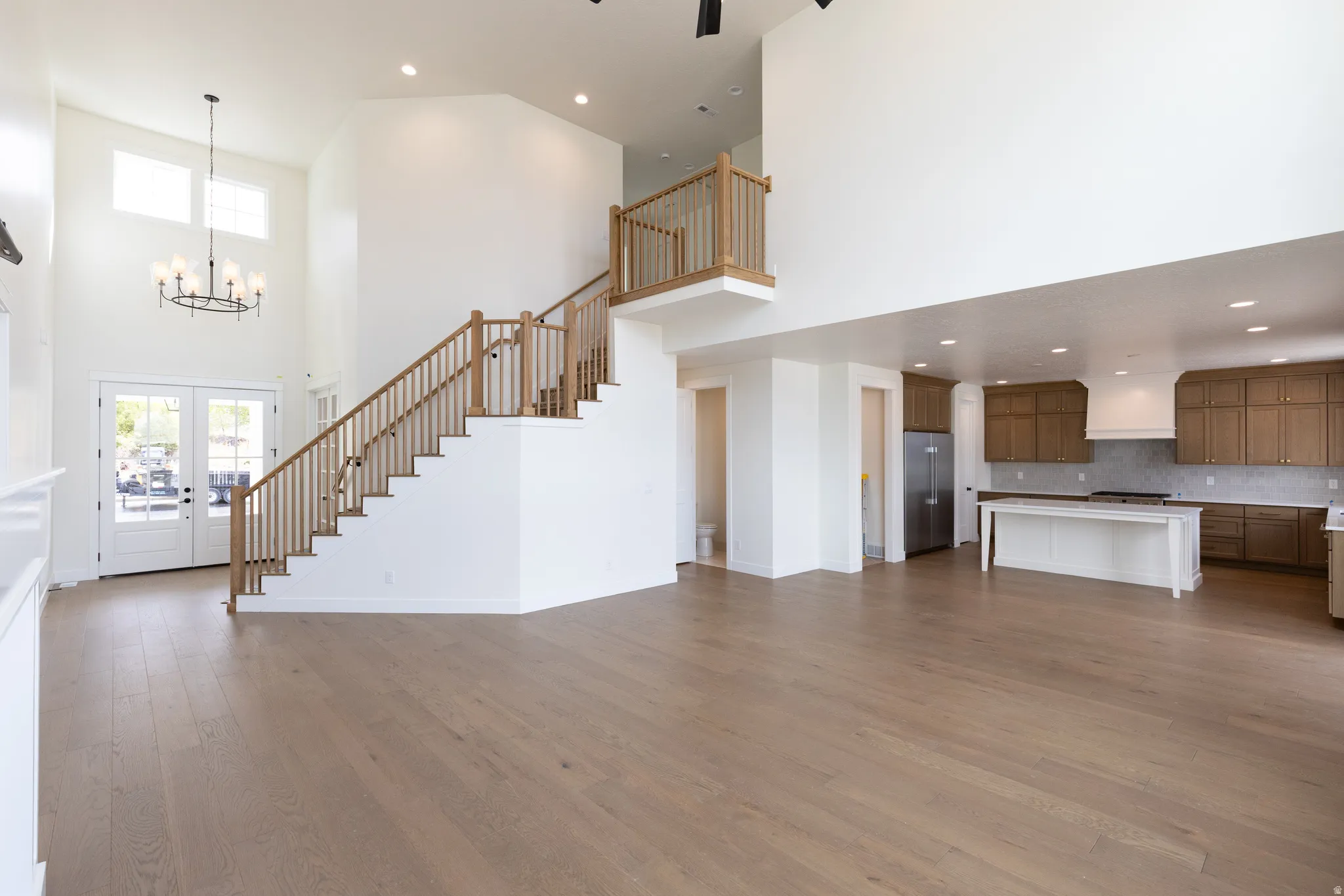 Spacious living area featuring high ceilings, wood-finish flooring, a grand staircase with wood railings, a contemporary chandelier, and an open-concept kitchen with wood cabinetry