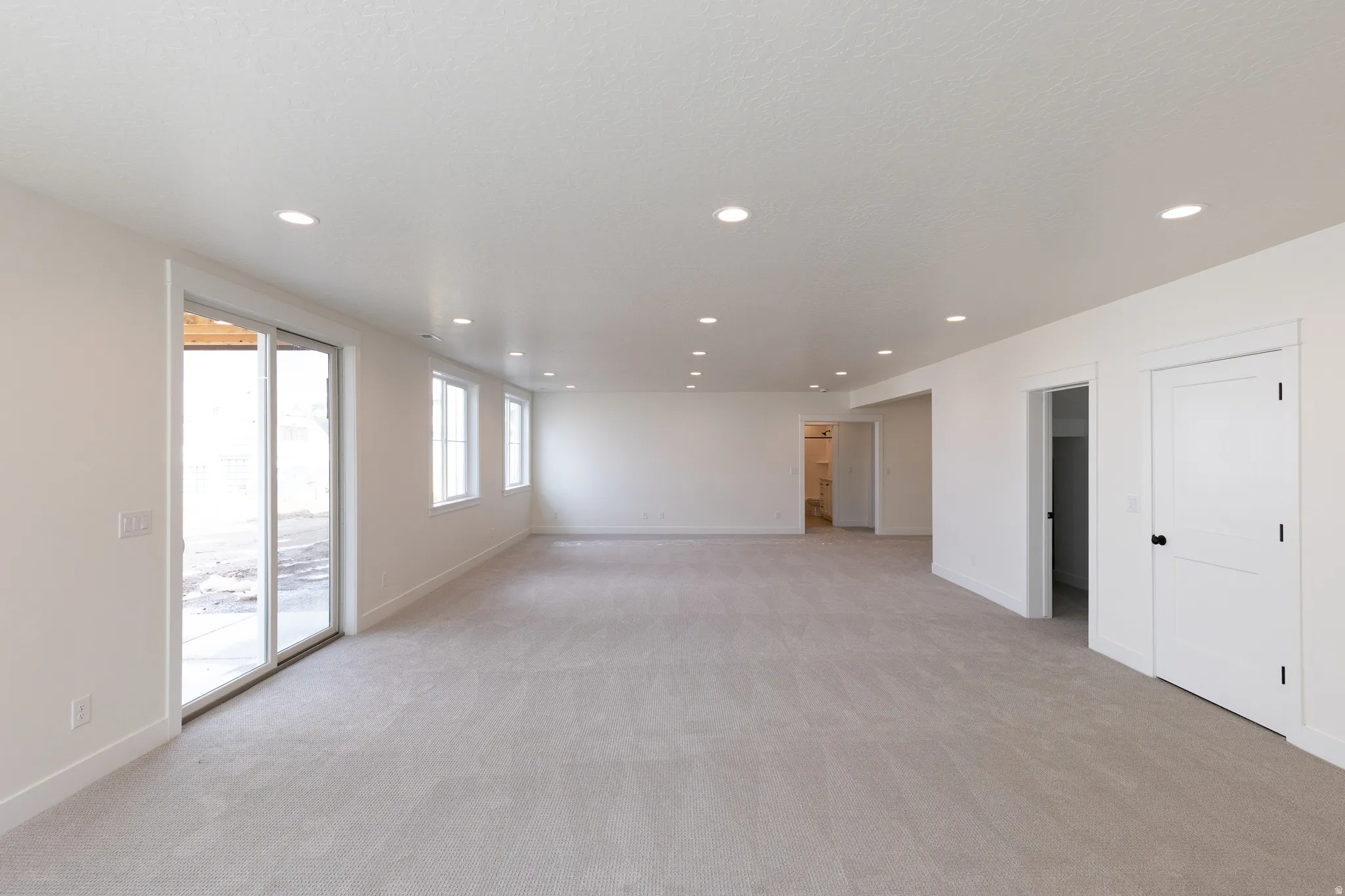 Spacious interior with neutral carpeting, recessed lighting, multiple windows, and a sliding glass door