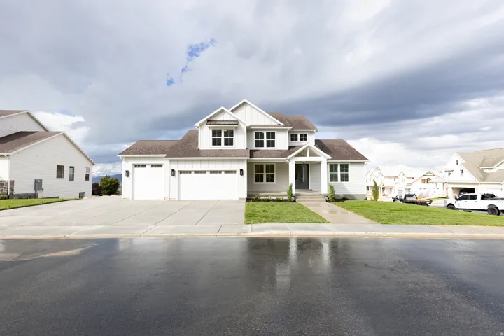 Modern farmhouse exterior with white vertical siding, dark roof shingles, two-car garage, and established front landscaping