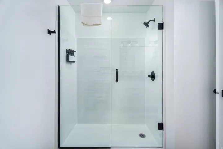 Glass-enclosed shower with matte black fixtures, subway tile surround, and a built-in shelf