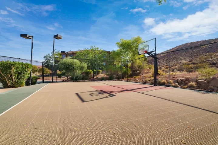 Multi-sport court featuring a basketball hoop with a clear backboard, durable modular surfacing, and dark perimeter fencing