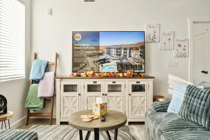 White entertainment console with glass-front cabinets and cross-paneled doors, topped with a large wall-mounted display