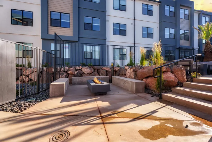Outdoor patio area featuring a built-in fire pit, concrete seating benches, and natural rock landscaping