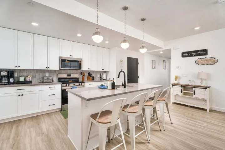 Bright kitchen featuring white cabinetry, stainless steel appliances, a light-toned backsplash, a central island with bar seating, and wood-finish flooring