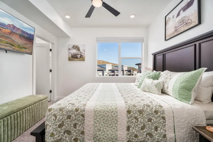 Bright bedroom featuring a large window, a dark wood-finish headboard, a ceiling fan with integrated lighting, recessed lighting, and a wall-mounted flat-screen television