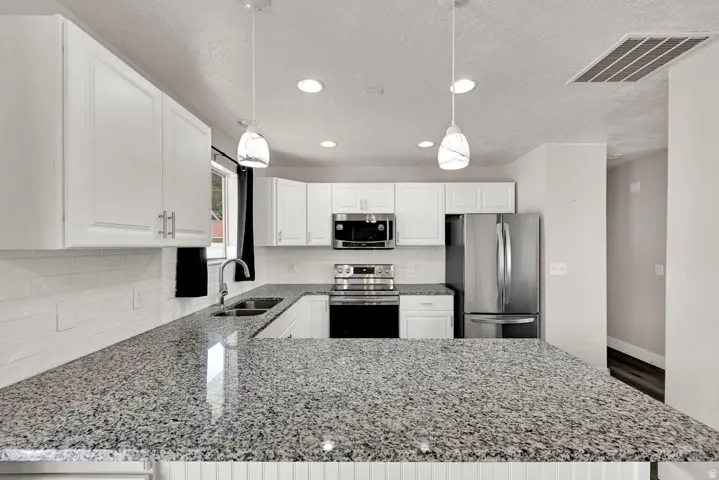Kitchen featuring white cabinetry, speckled countertops, stainless steel appliances, and a subway tile backsplash