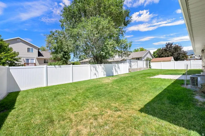 Expansive lawn area surrounded by white privacy fencing, featuring a concrete patio pad