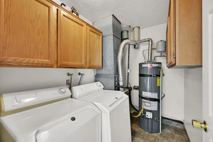 Utility space featuring wood-finish cabinetry, a hot water heater, and durable flooring