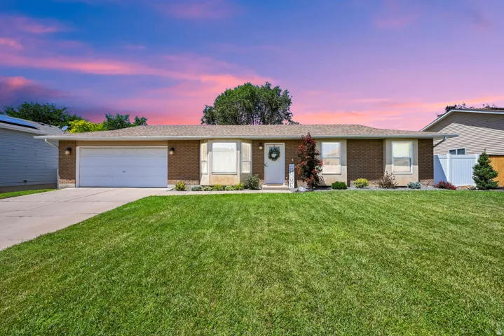 Mid-century modern brick rambler featuring an attached two-car garage, established landscaping, bay window, and a white entry door