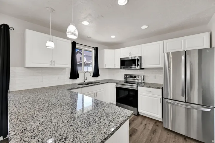Kitchen featuring white shaker cabinetry, stainless steel appliances, speckled stone countertops, a subway tile backsplash, and wood-finish flooring