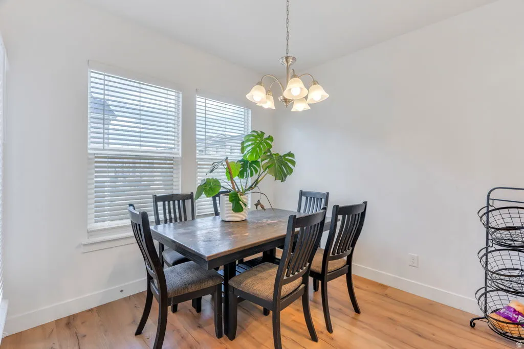 Dining area featuring two large windows with blinds, wood-finish flooring, a contemporary chandelier, and crisp white walls
