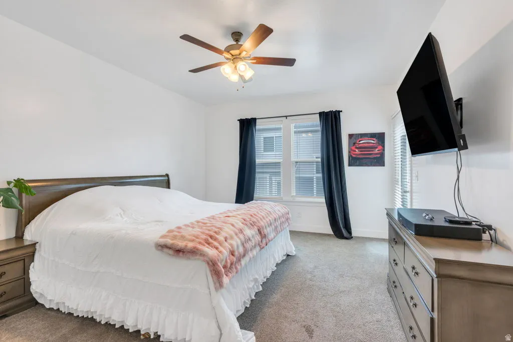 Carpeted room featuring a ceiling fan with light fixture, a window with blinds and dark curtains, and a glass-paneled door