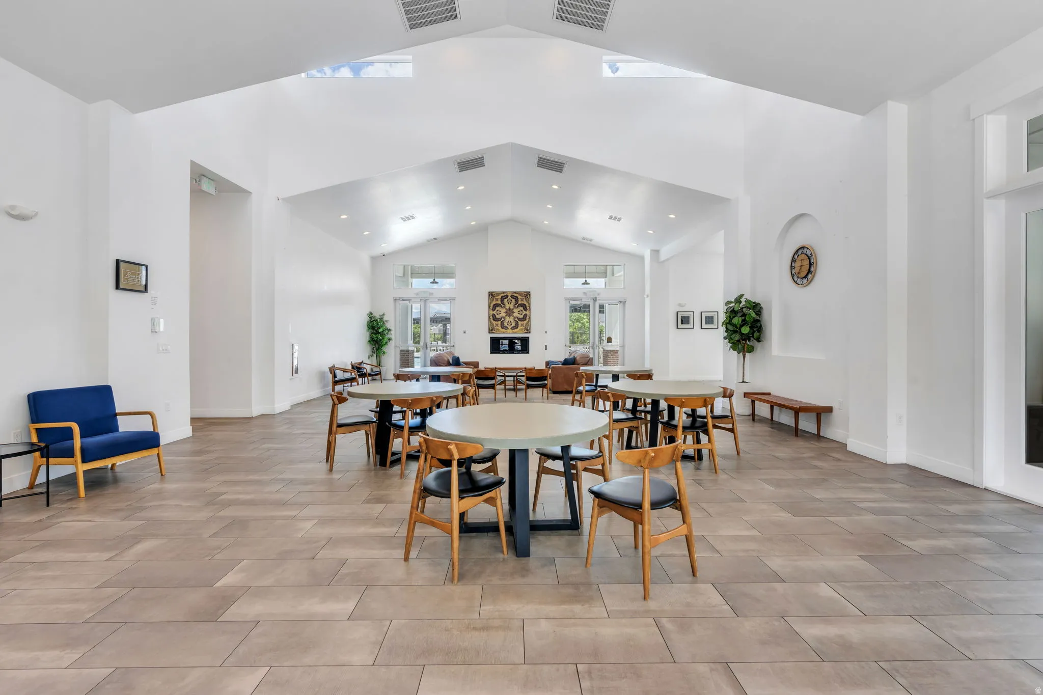 Spacious room featuring vaulted ceilings, light-tone tile flooring, multiple seating areas, and an integrated fireplace