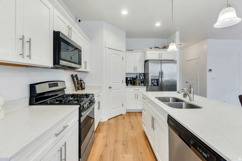 Modern kitchen featuring white cabinetry, light-toned countertops, wood-finish flooring, stainless steel appliances, and a central island with an undermount sink