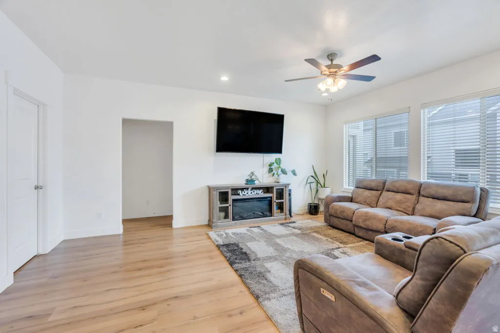 Spacious living area featuring wood-finish flooring, a ceiling fan with integrated lighting, and multiple windows with blinds
