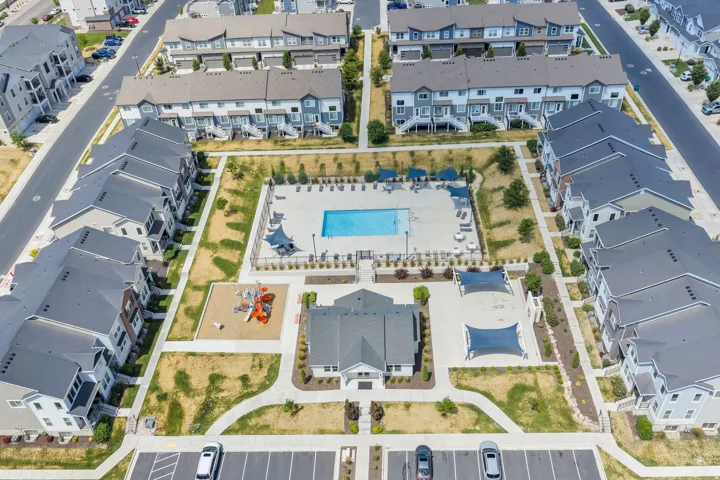 Community grounds featuring a central swimming pool, a clubhouse building, a playground, and shaded outdoor areas