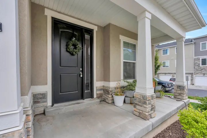 Covered front porch with decorative stone accents, robust white pillars, and a paneled black entry door