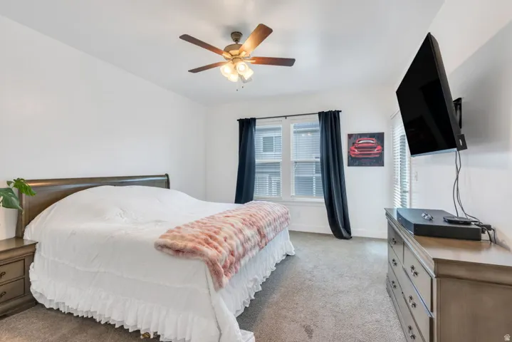 Carpeted room featuring a ceiling fan with light fixture, a window with blinds and dark curtains, and a glass-paneled door