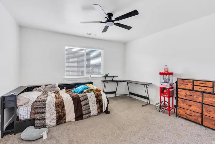Carpeted room featuring a ceiling fan with integrated lighting, a window with horizontal blinds, and a built-in bed frame with integrated shelving