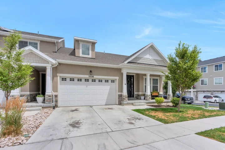 Contemporary exterior featuring a covered front porch, stone accents, two-car garage, and dormer window