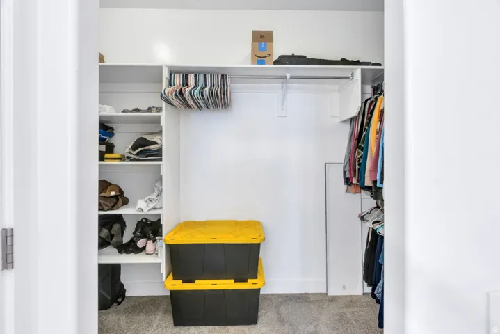 Built-in closet system featuring white shelving, multiple hanging rods, and light gray carpeting