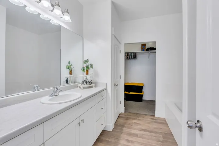 Bathroom featuring an extended vanity with an integrated sink, broad wall mirror, and overhead vanity lighting