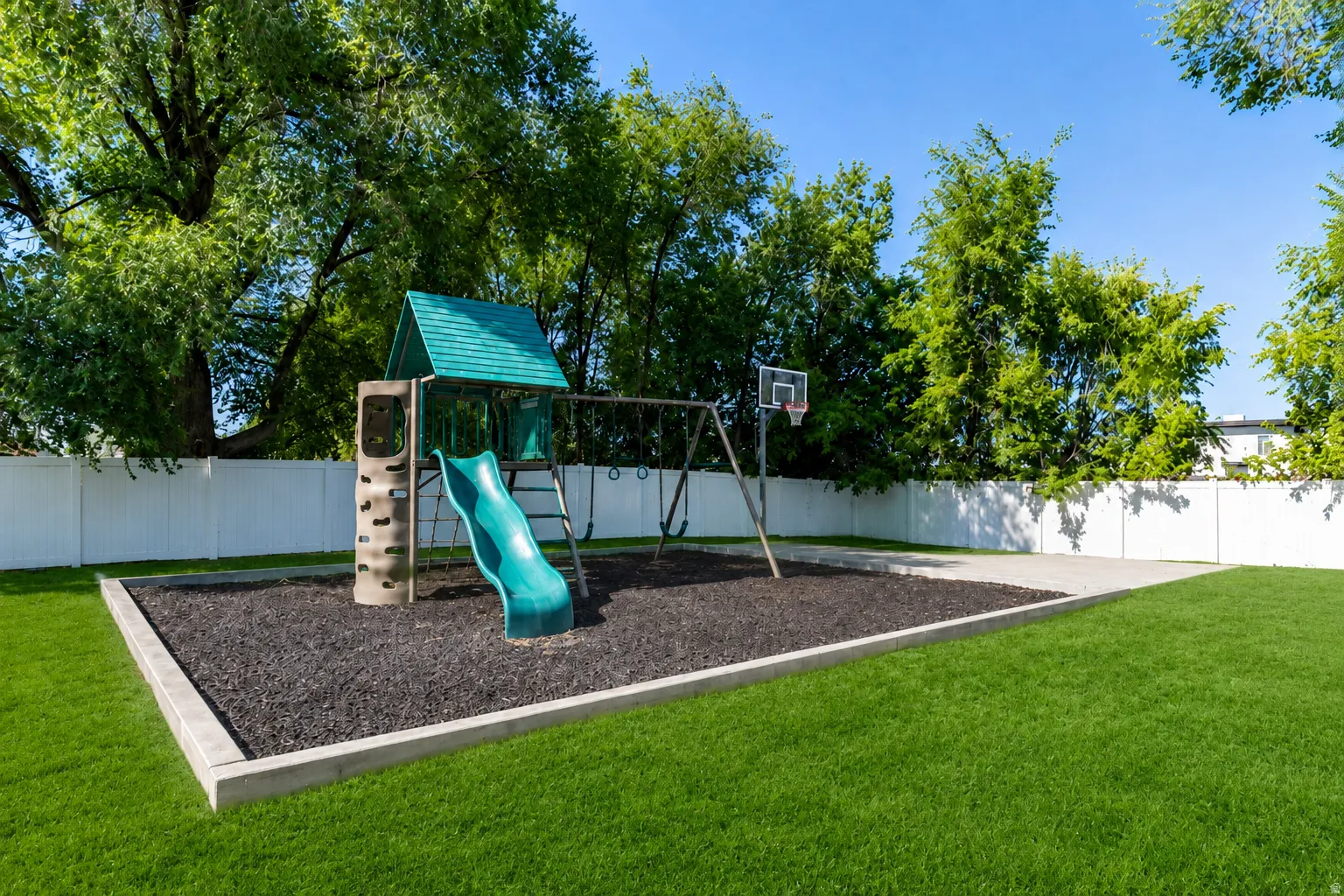 Expansive backyard featuring a dedicated play area with a playset and basketball hoop