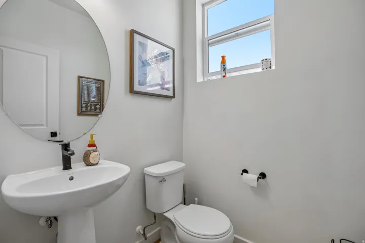 Modern powder room featuring a white pedestal sink with a matte black faucet, a round wall-mounted mirror, and a white toilet