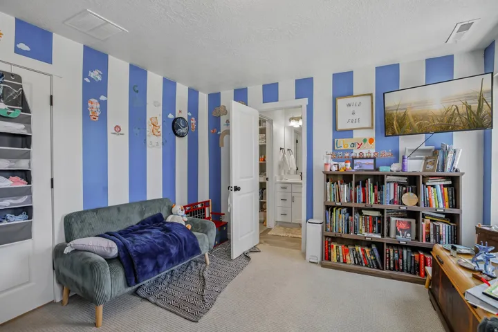 Carpeted room featuring a built-in bookshelf, a mounted television, and a doorway opening to a bathroom with a vanity and mirror