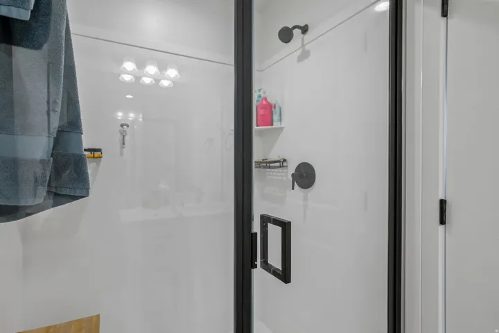 Modern shower enclosure featuring a black-framed glass door, matte black shower fixtures, a built-in shower shelf, and white shower walls