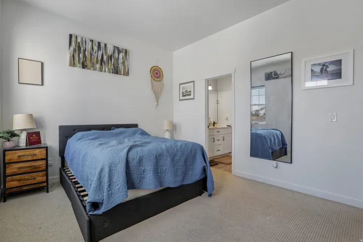 Carpeted bedroom with white walls and an open doorway revealing a bathroom with a white vanity and light-colored countertop