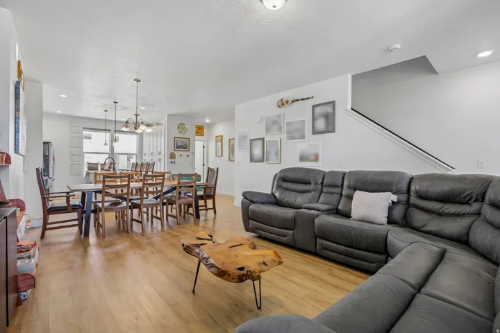 Open-concept living space featuring wood-finish flooring, recessed lighting, a staircase with a dark handrail, and a dining area with pendant lighting