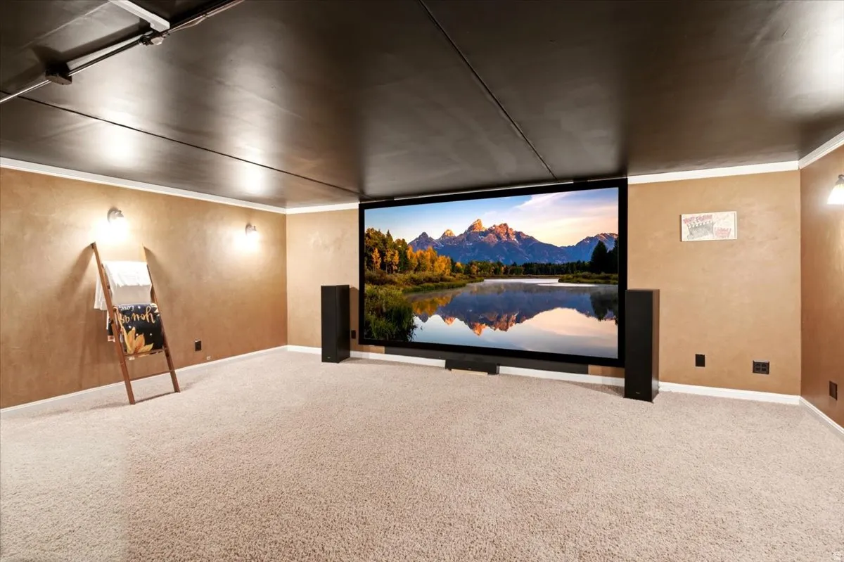 Dedicated entertainment space featuring a large projection screen, wall-mounted sconces, and neutral-toned carpeting