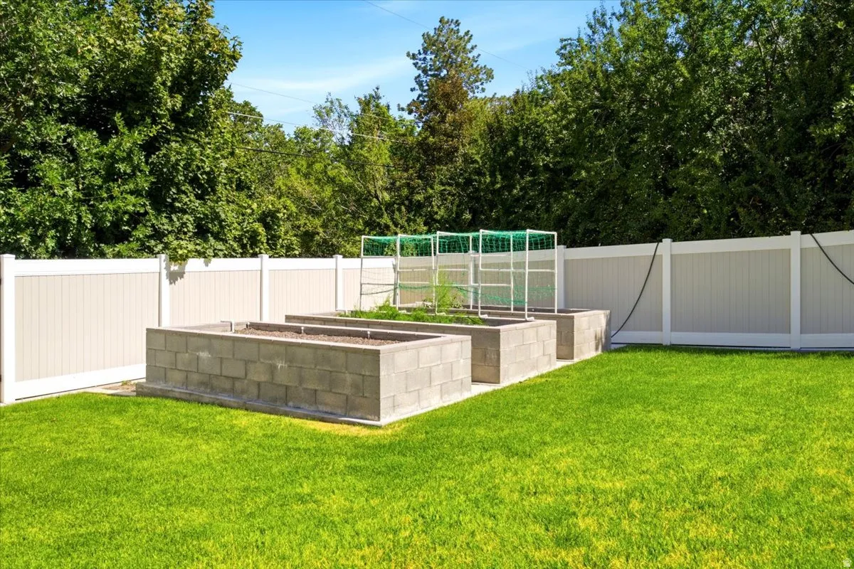 Expansive backyard featuring a lush lawn, two raised garden beds constructed from concrete blocks, and a privacy fence