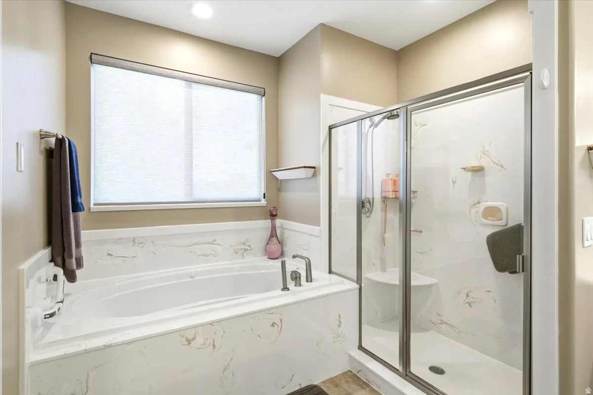 Bathroom featuring a built-in soaking tub with a patterned surround, a separate glass-enclosed shower with a built-in bench, and a window with a roller shade