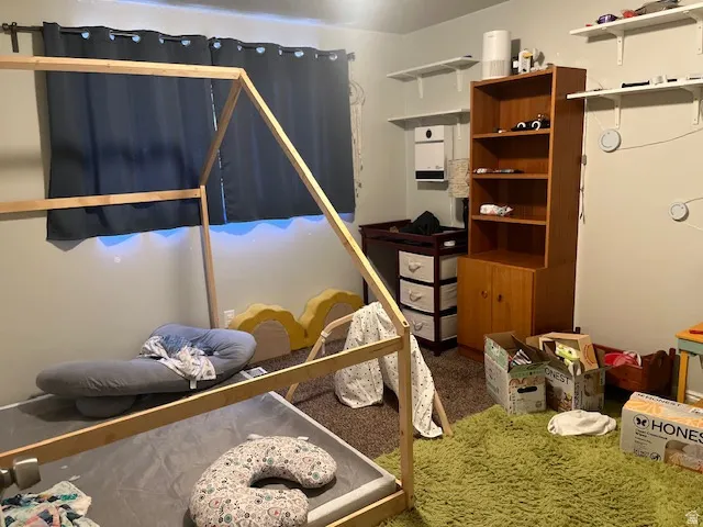 Carpeted room featuring a window with dark curtains, built-in shelving, a wood-finish bookcase with cabinet storage, and white floating wall shelves