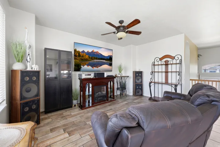 Living area featuring wood-finish tile flooring, a ceiling fan with integrated lighting, and white wall finishes