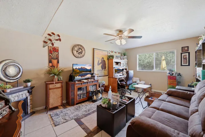 Living area featuring a light-toned tile floor with contrasting dark tile accents, a window with blinds, and a ceiling fan