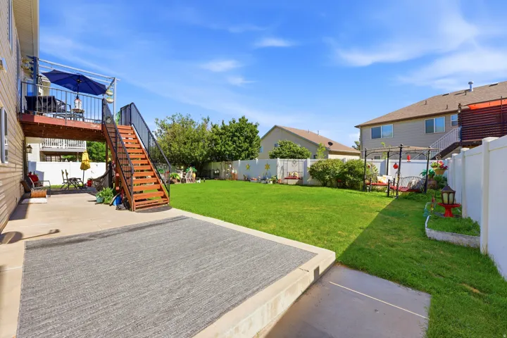 Spacious backyard featuring a substantial lawn, concrete patio, and a raised wood-finish deck with black metal railings