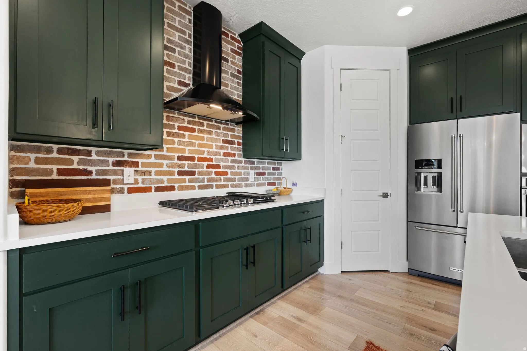 Kitchen featuring dark green cabinetry, white countertops, brick-style backsplash, stainless steel appliances, and wood-finish flooring
