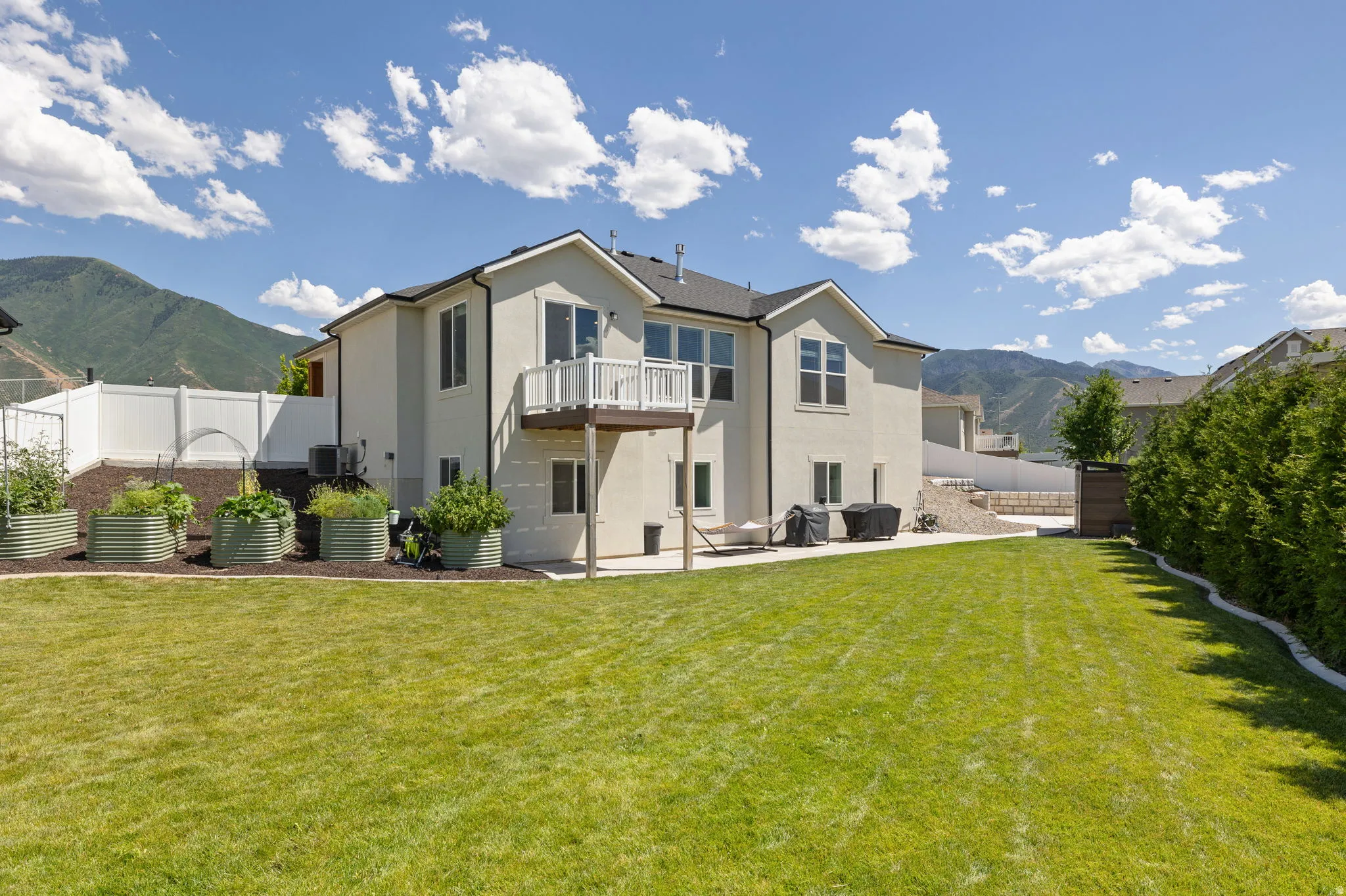 Expansive backyard featuring a manicured lawn, a concrete patio, and a second-story balcony with white railing