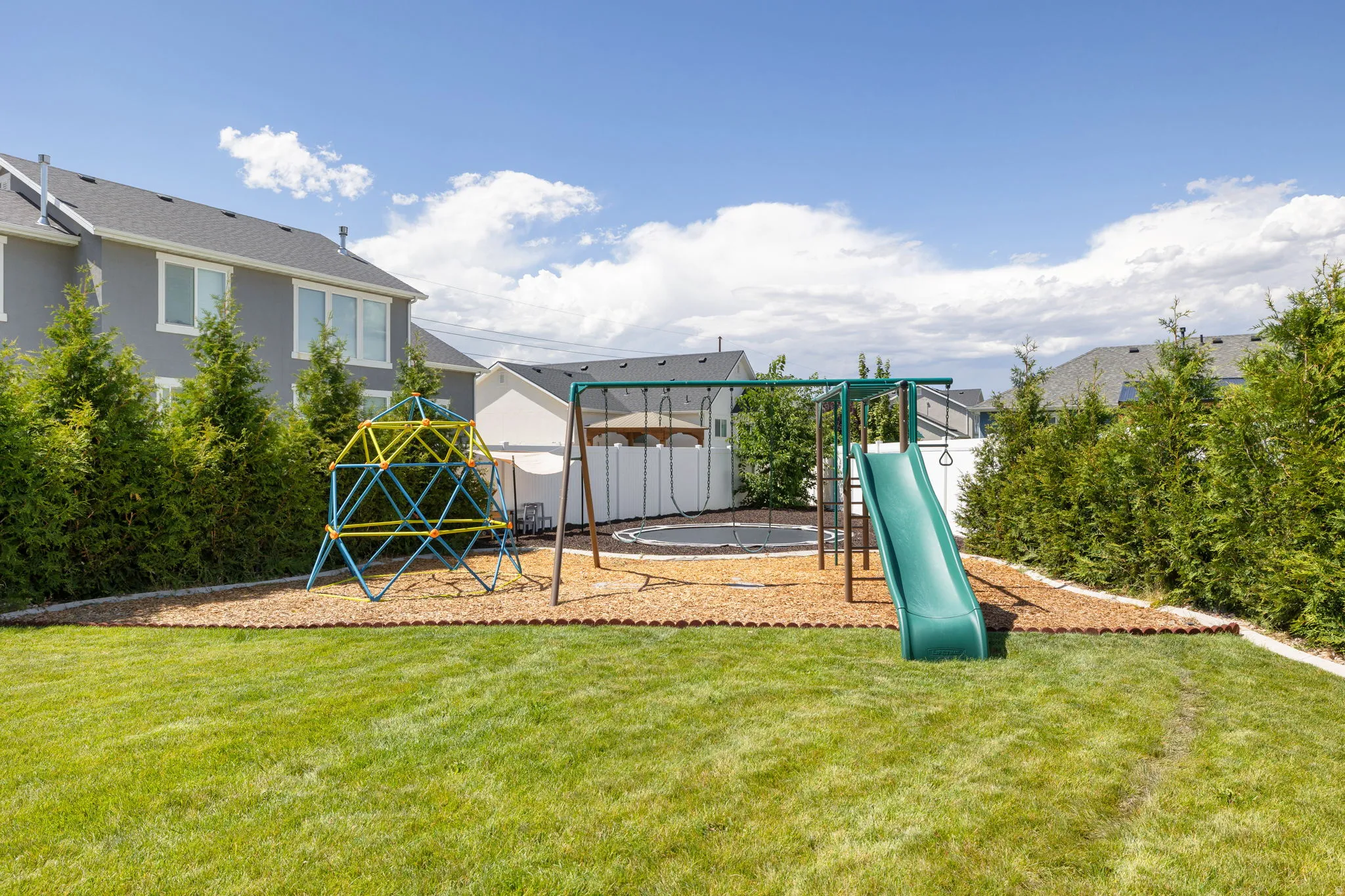 Expansive backyard featuring a green lawn, mature perimeter shrubbery, and a designated play area with wood chip ground cover