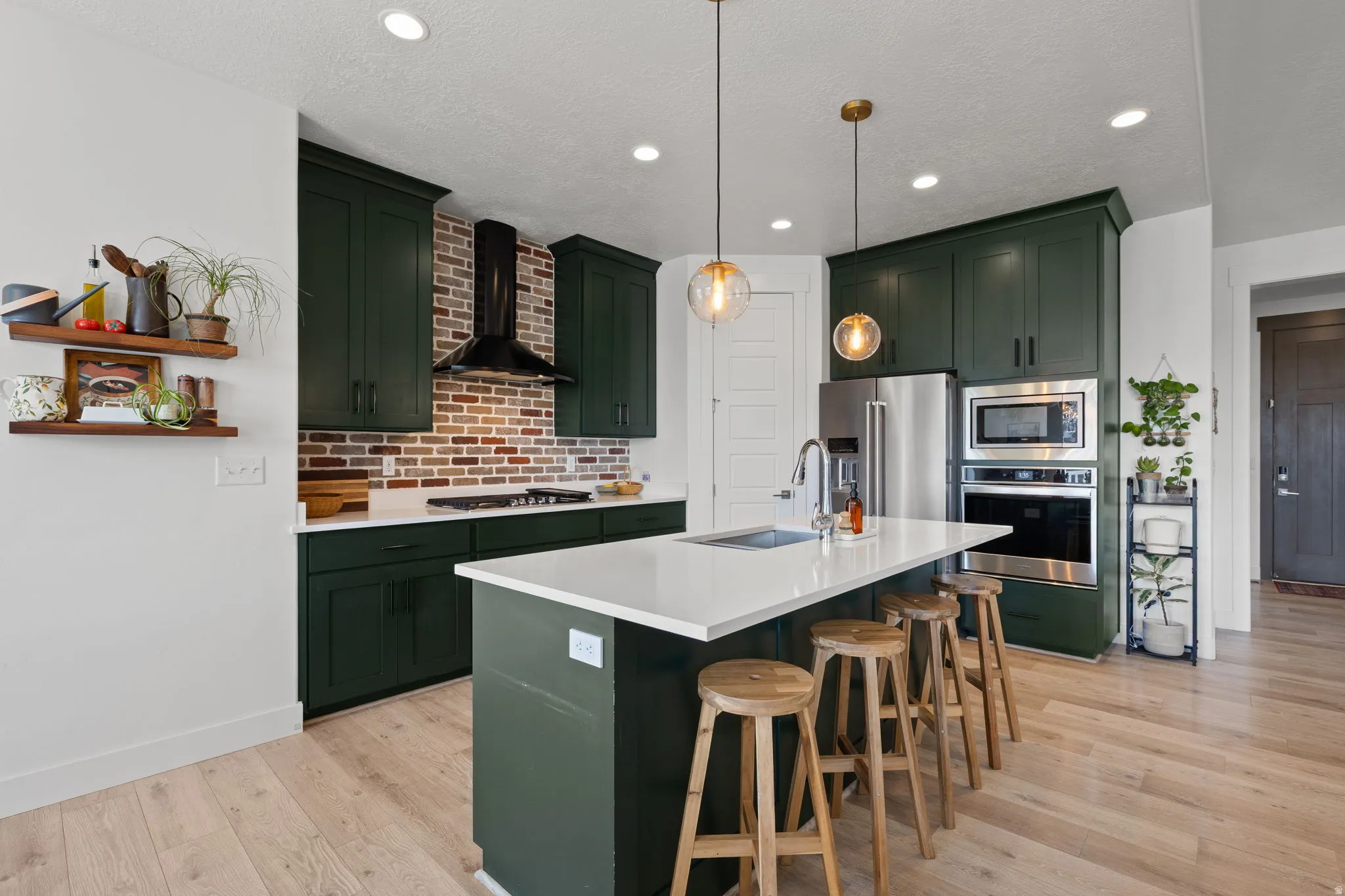 Kitchen featuring deep green cabinetry, white countertops, wood-finish flooring, a brick-style backsplash, and stainless steel appliances