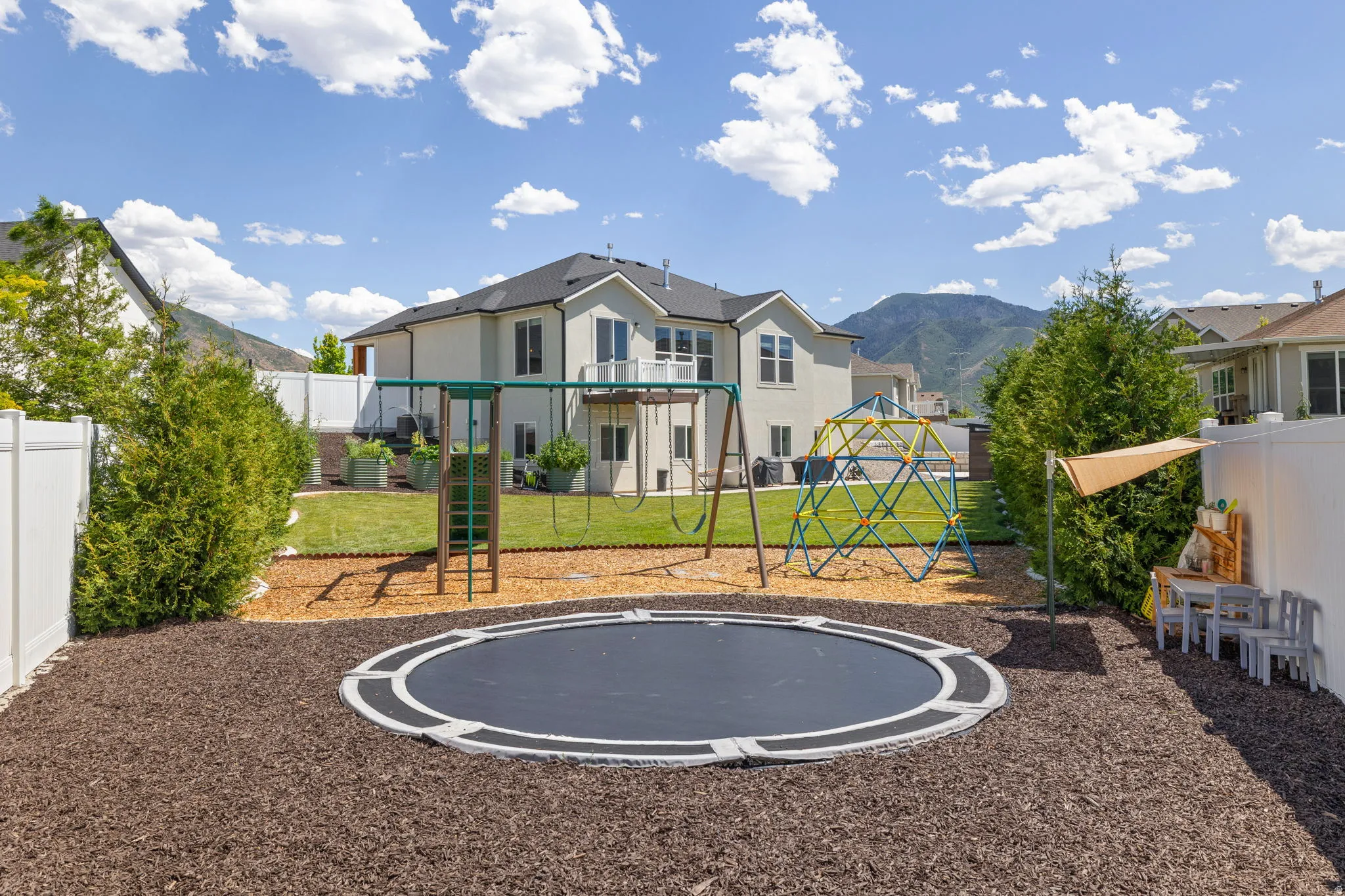 Spacious backyard featuring a manicured lawn, white privacy fencing, mature landscaping, and a mountain backdrop